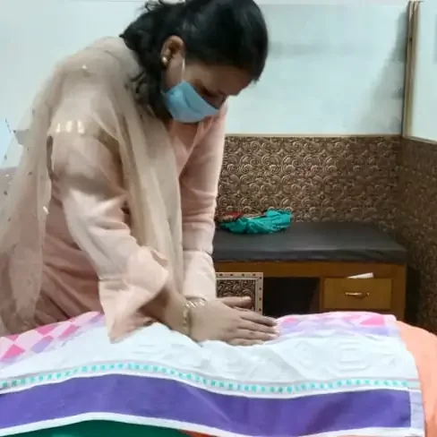 A masked physiotherapist treating a patient lying on a treatment plinth.