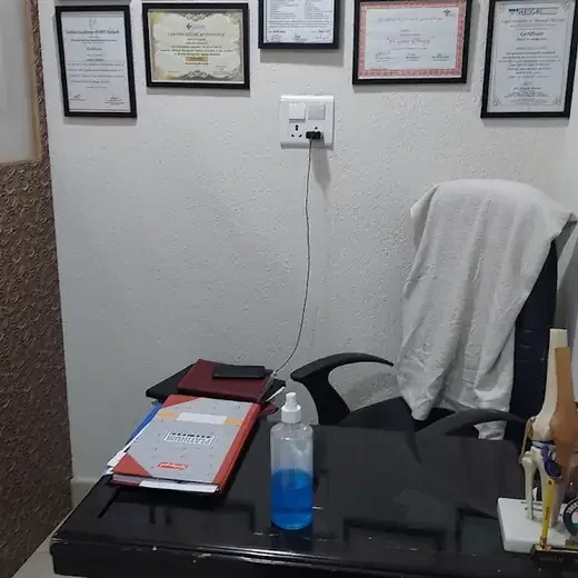 Framed certificates on the wall above a desk with an office chair, a towel and a hand-sanitizer bottle.